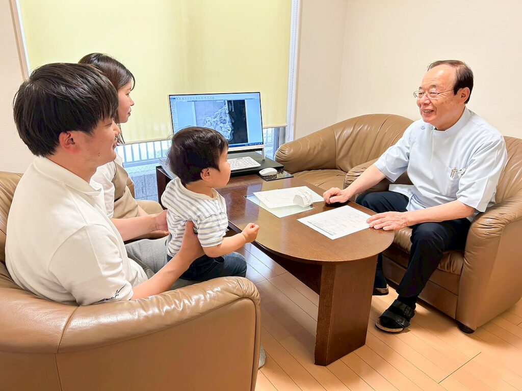 矯正治療について相談にきている親子と話をする鯨井正夫院長の写真